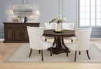Modern round dark wood dining table with upholstered cream chairs in a bright dining room