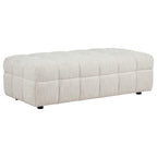 Cream quilted upholstered ottoman with channel-tufted design and black legs on white background.