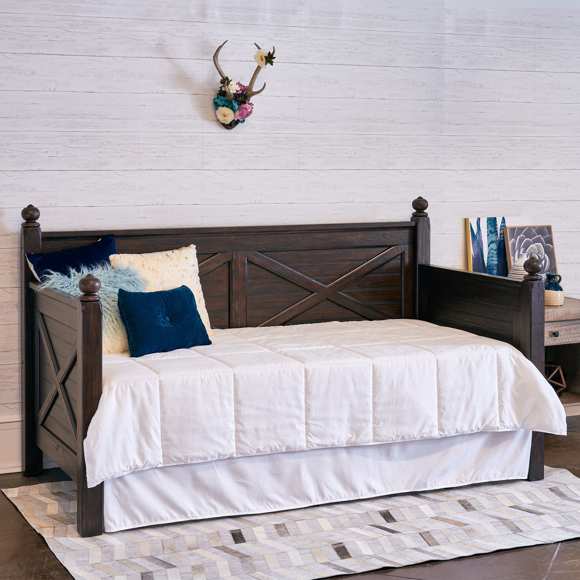 Twin wood daybed in walnut finish with X-design panels, white quilted bedding, rustic dark wood frame.